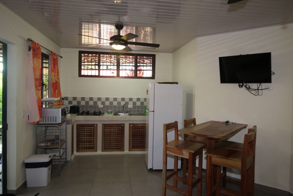 dining area with tv and kitchen of Casa Nela, hotel and rental income property for sale at Samara Beach, Guanacaste, Costa Rica