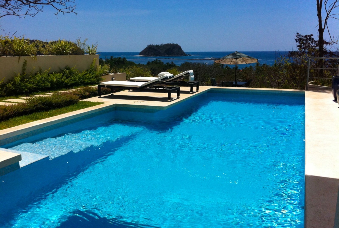 Large blue pool with two beach chairs and at the back the ocean and Isla chora Samara Reef Condo for sale Samara Guanacaste Costa Rica