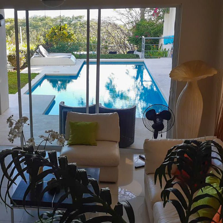 two sofas with coffe table, green plants glass glass door open to the pool Samara Reef Condo for sale Samara Guanacaste Costa Rica