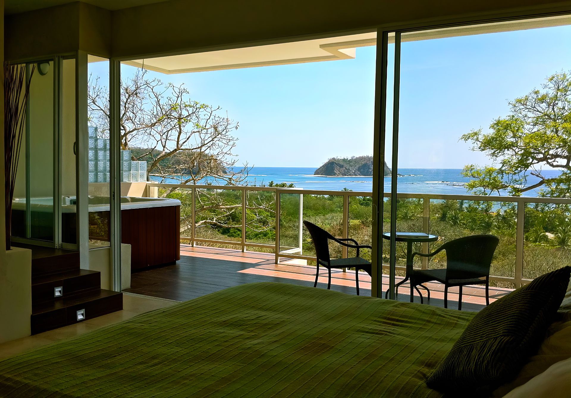King sized bed with green bedspread with balcony jacuzzi and 2 chairs and table looking the ocean Samara Reef Condo for sale Samara Guanacaste Costa Rica