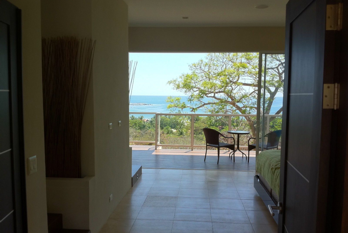 Door open showing a piece of bed and a balcony with 2 chairs and a table with ocean view Samara Reef Condo for sale Samara Guanacaste Costa Rica