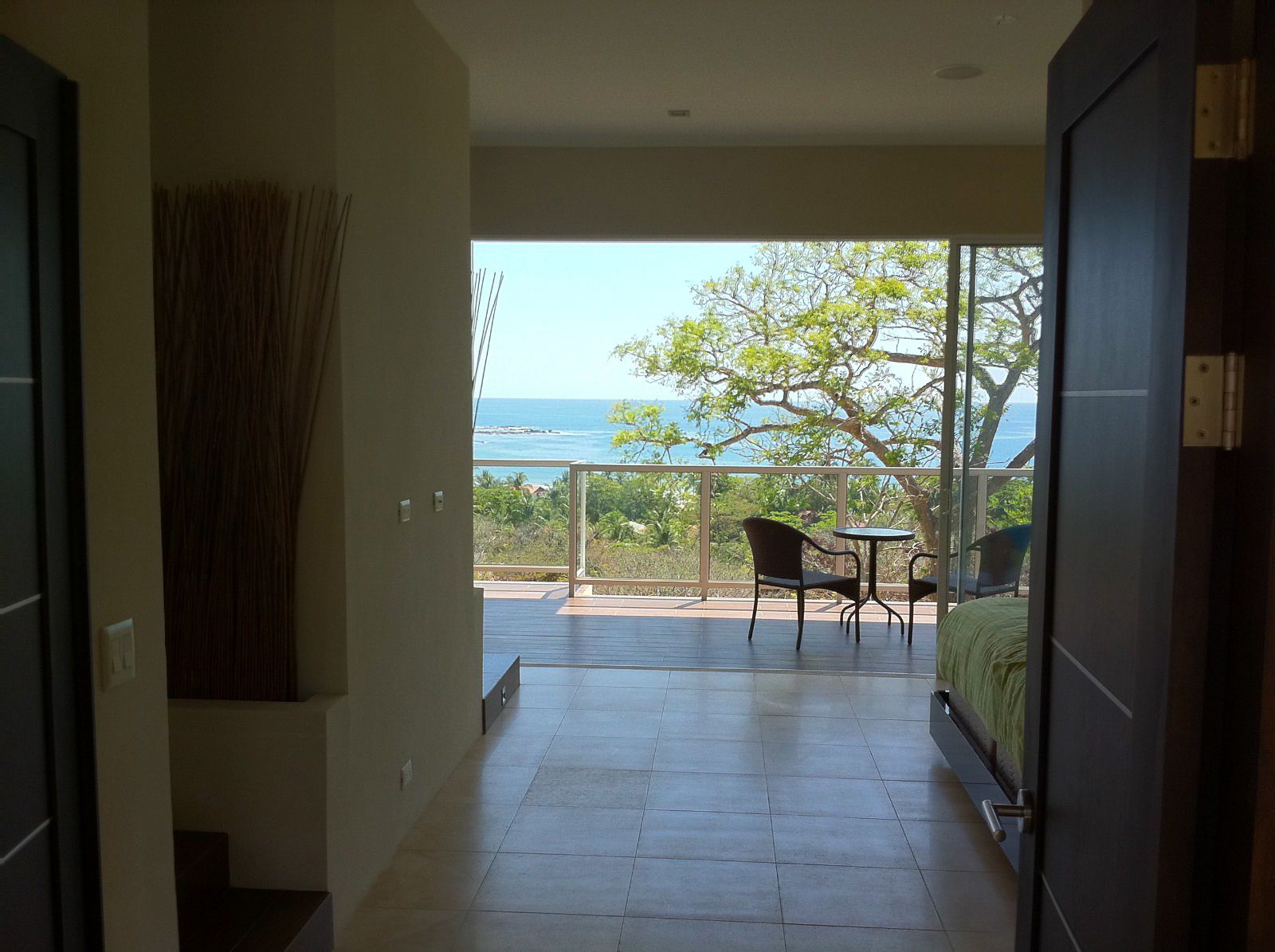 Door open showing a piece of bed and a balcony with 2 chairs and a table with ocean view Samara Reef Condo for sale Samara Guanacaste Costa Rica