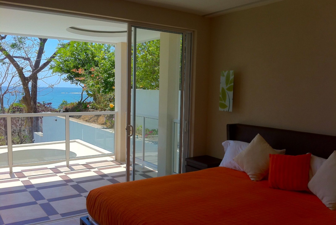 Queen sized bed with orange bedspread balcony overlooking the ocean Samara Reef condo for sale Samara Guanacaste Costa Rica